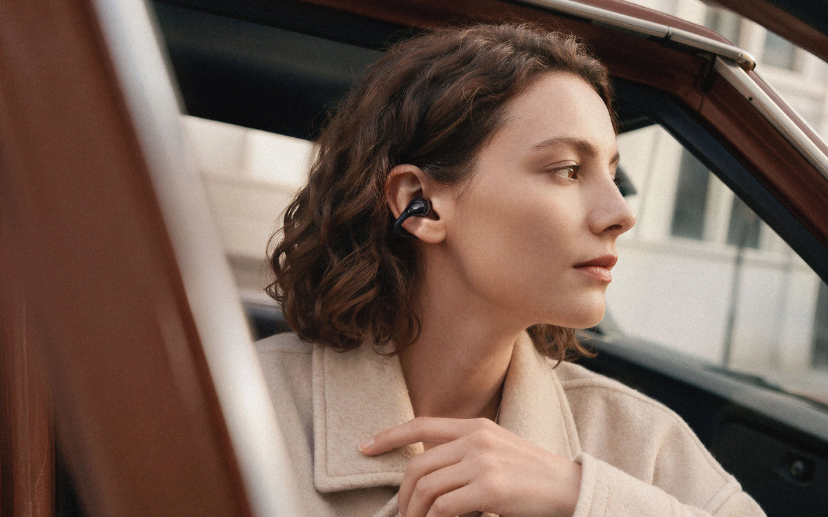 Woman wearing C-Flow earbuds beside a car