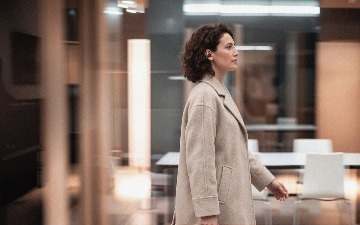 Woman wearing C-Flow earbuds walking through a modern interior
